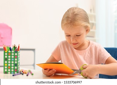 Little Left-handed Girl Cutting Construction Paper At Table