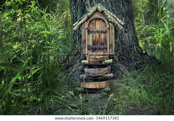 Little magic wooden fairy door in tree\
trunk, mystery forest natural background. Fairytale tree house in\
beautiful green woodland, pixie and elf\
home