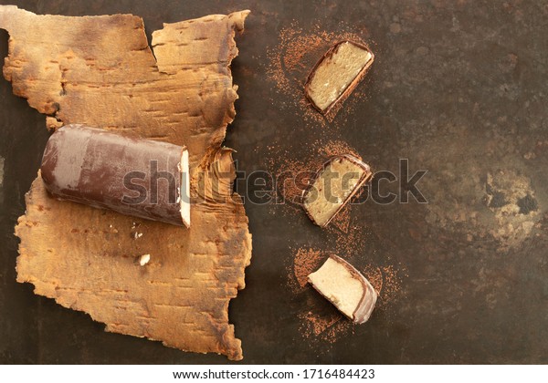 Little marzipan bar covered with chocolate lying on\
birch bark with three separate pieces of it besides on dark\
background with copy space  \
