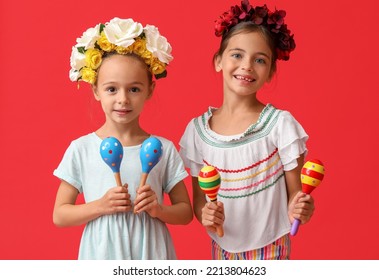Little Mexican Girls With Floral Wreaths And Maracas On Red Background