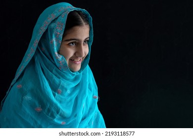 Little Muslim Girl With Beautiful Eyes Wearing Blue Hijab Smiling With Someone, Black Background, Side View