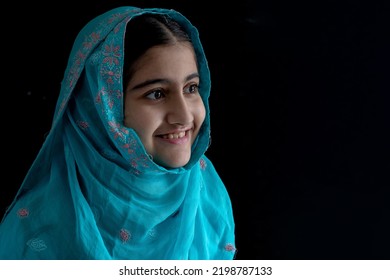 Little Muslim Girl With Beautiful Eyes Wearing Blue Hijab Smiling With Someone, Black Background, Side View