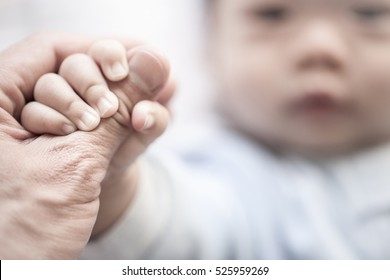 Little newborn baby holding parent's one hand, close-up macro shot. Focus on foreground. The touching and lovely moment. Concept of support, hope, love, bonding and care, hold on...