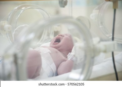 Little Newborn baby in incubator. Adorable infant in yellow hats wrapped in blue cloth in delivery room.