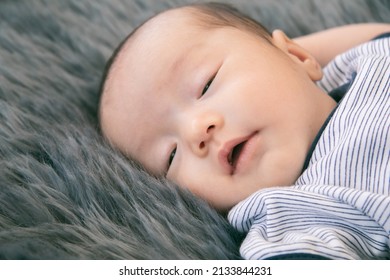 Little Newborn Baby Sleeping On Gray Fur Bed With Happy, Adorable Infant Wear Blue Casual Clothes Lying In Bedroom With Feel Safe. Asian Toddler Sleep On His Back Relaxing On Bed. Nursery For Children