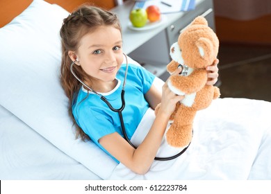 Little Patient With Stethoscope And Teddy Bear Lying On Bed In Hospital