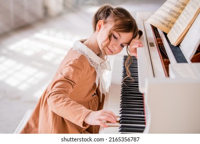 Little Pensive Girl Plays The Big White Piano In Bright Sunny Room