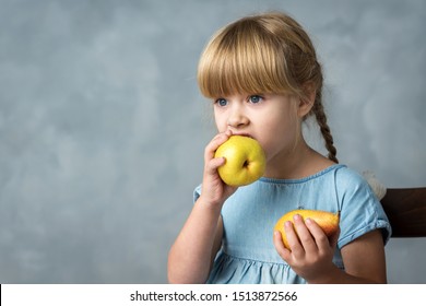 little pigtailed girl in blue dress playing with two ripe pears