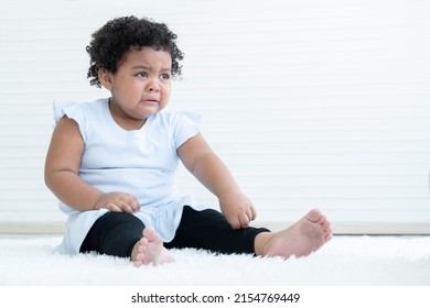 Little pitiful African American chubby kid girl is crying with tears drop from eyes while sitting on fluffy carpet on floor at home. Child emotion care concept. White background. Copy space