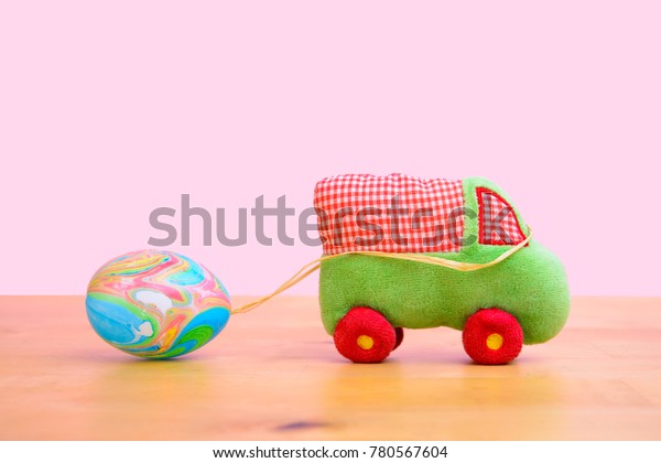 little plush car with Easter egg  in front of\
pink background