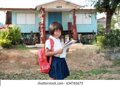 A little poor girl in school uniforms carry broken bag reading a book at school