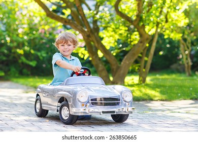 Little preschool boy driving big toy old vintage car and having fun, outdoors. Active leisure with kids on warm summer day.