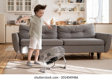 Little Preschool Boy Enjoy Fresh Air Flow From Fan. Cute Small Kid Play With Ventilator Blowing Cool Wind Alone In Living Room At Home. Cute Child Have Fun Indoors In Apartment One. Childhood Leisure