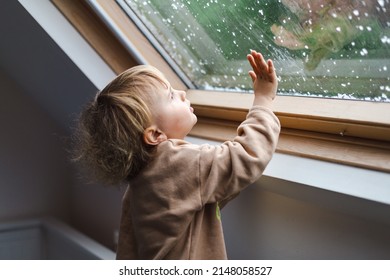 Little preschool boy staying home in bad weather and looking  with interest through window on raindrops and hail, idoors. - Shutterstock ID 2148058527
