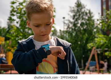 A Little Preschool Boy Walks On One Street. The Child Calls The Smart Watch. The Boy Walks On The Street With A Smith Watch