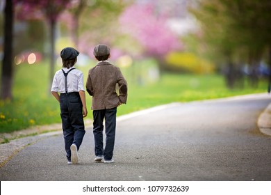 Little preschool boys, cute children, brothers, dressed in vintage style clothes, in a park under blooming trees, looking fashionable, walking away on a path