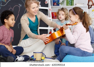 Little Preschool Girl Holding Teacher's Guitar On Music Lesson