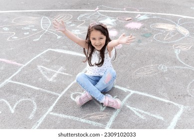 Little preschool girl painting  and colorful chalks ground   Positive happy toddler child drawing   creating pictures  Creative outdoors activity in summer