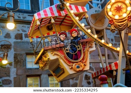 Little preschool girl and school boy riding on ferris wheel carousel horse at Christmas funfair or market, outdoors. Two happy children having fun on traditional family xmas market in Germany