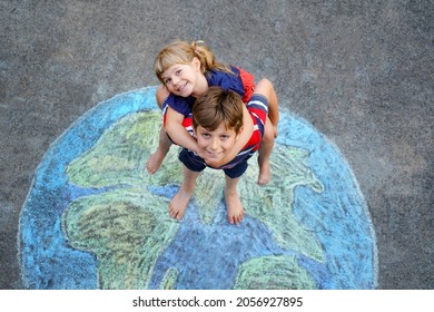 Little preschool girl and school kid boy with earth globe painting with colorful chalks on ground. Happy earth day concept. Creation of children for saving world, environment and ecology.