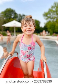 Little Preschool Girl Splashing In An Outdoor Swimming Pool On Warm Summer Day. Happy Healthy Toddler Child Enjoying Sunny Weather In City Public Pool. Kids Activity Outdoors With Water.