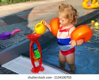 Little Preschool Girl Splashing In An Outdoor Swimming Pool On Warm Summer Day. Happy Healthy Toddler Child Enjoying Sunny Weather In City Public Pool. Kids Activity Outdoors With Water.