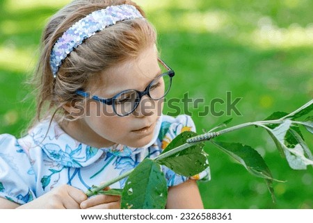 Little preschool girl watches caterpillar climb on plant. Happy excited child watching and learning insects in domestic gardens.