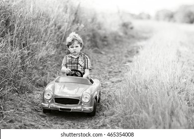 Little preschool kid boy driving big toy car and having fun with playing, outdoors. Child enjoying warm summer day in nature landscape. Old picture in black and white.