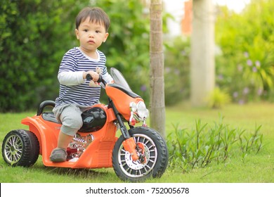 Little preschool kid boy driving orange motorbike toy at home.