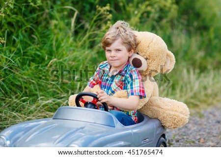 Little preschool kid boy driving big toy car and having fun with playing with his plush toy bear, outdoors. Child enjoying warm summer day in nature landscape
