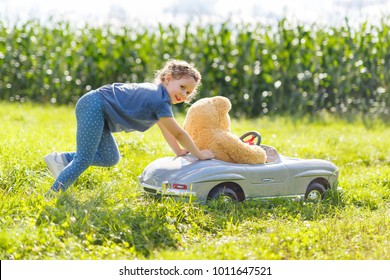 Little Preschool Kid Girl Driving Big Toy Car And Having Fun With Playing With Big Plush Toy Bear