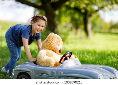 Little Preschool Kid Girl Driving Big Toy Car And Having Fun With Playing With Big Plush Toy Bear