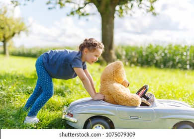 Little Preschool Kid Girl Driving Big Toy Car And Having Fun With Playing With Big Plush Toy Bear