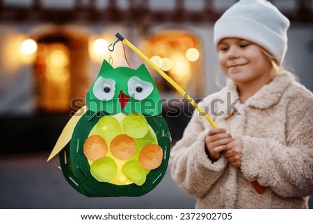 Little preschool kid girl holding selfmade traditional owl lanterns with candle for St. Martin procession. child happy about children and family parade in kindergarten. German tradition Martinsumzug