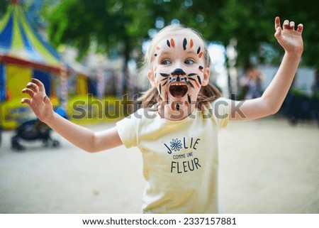 Little preschooler girl with tiger face painting outdoors. Children face painting. Creative activities for kids
