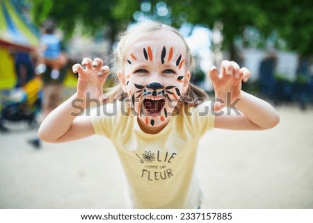 Little preschooler girl with tiger face painting outdoors. Children face painting. Creative activities for kids