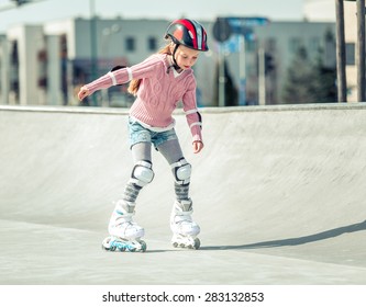 Little pretty girl on roller skates in helmet at a park