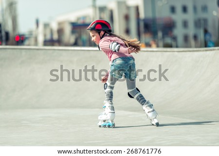 Little pretty girl on roller skates in helmet at a park. back view