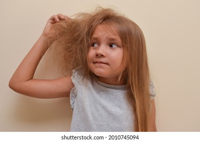 A little pretty girl with an open mouth in horror holds with her hand half of her hair, which is very tangled, the other half of her hair is combed and lies silky.  Child shocked by a mess on the head