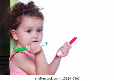 Little pretty girl standing near the blackboard and space for text   holds markets in both hands  child looking at the camera 