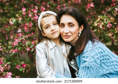 little pretty girl toddler armenian daughter and mother beautiful middle aged woman walk in an apple blossoming pink garden, family portrait in a spring park among flowering blooming trees