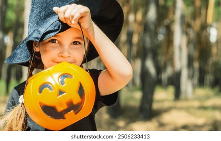 Little pretty girl in witch costume holding jack-o-lantern pumpkin bucket with candies and sweets. Kid trick or treating in Halloween holiday - Powered by Shutterstock