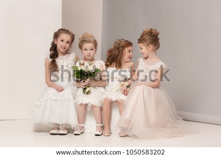 Little pretty girls with flowers dressed in wedding dresses. Lovely little girlfriends. girls dreaming of a wedding. Beauty, happiness, marriage, wedding style concepts. Studio shot