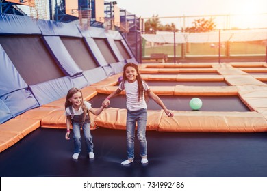 Little pretty girls having fun outdoor. Jumping on trampoline in children zone. Amusement park