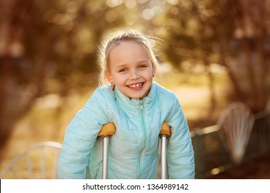 Little pretty smiling girl in blue jacket using crutches on sunny spring day - Powered by Shutterstock