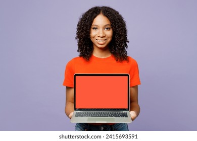 Little programmer kid teen IT girl of African American ethnicity she wear orange t-shirt work hold use blank screen laptop pc computer isolated on plain purple background. Childhood lifestyle concept - Powered by Shutterstock