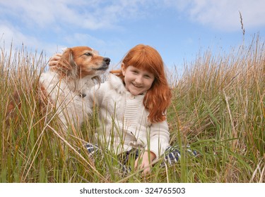 little red haired girl with red haired collie type dog sitting among long dune grass on a sand dune at a surf beach, near Gisborne, East Coast, North Island, New Zealand 
