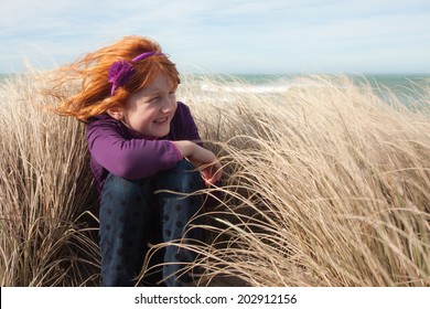 little red haired girl in long grass on a sand dune at the beach on a windy day 