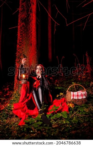 Little Red Riding Hood halloween costume in dark forest holding lantern in red raincoat and scar on her face