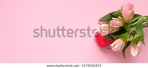 little red toy car carries a bouquet of pink\
flowers on a pink\
background.
